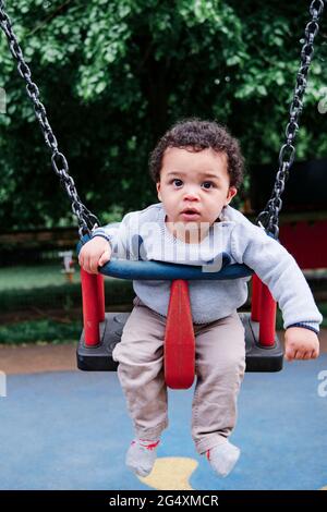 Carino bambino che dondola sul swing nel parco giochi Foto Stock