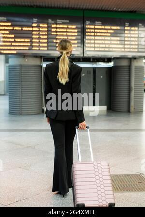 Assistente di volo femminile che cammina con valigia all'aeroporto Foto Stock