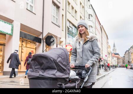 Madre che spinge il passeggino mentre cammina sulla strada in città Foto Stock