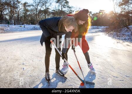 Ragazza con ragazzo che gioca a hockey su ghiaccio sul lago ghiacciato Foto Stock