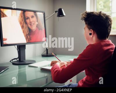 Ragazzo che indossa le cuffie e-learning durante la videochiamata sul computer a casa Foto Stock