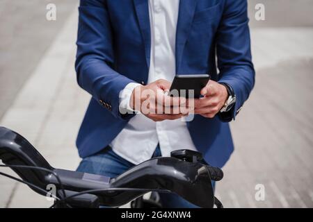 Uomo d'affari con bicicletta elettrica noleggiata utilizzando il telefono cellulare sul sentiero Foto Stock