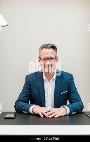 Uomo d'affari sorridente che indossa occhiali seduti in ufficio Foto Stock