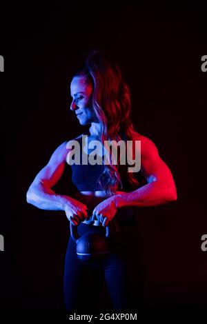 Donna muscolosa che tiene kettlebell su sfondo nero Foto Stock