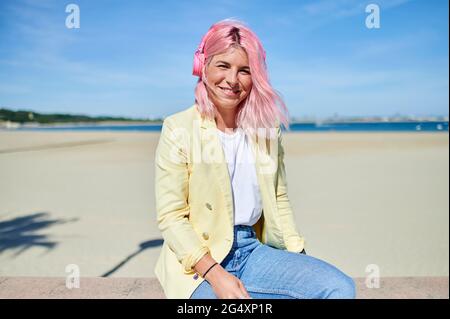 Donna sorridente che ascolta la musica attraverso le cuffie mentre si siede sulla ringhiera a Promenade Foto Stock