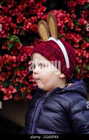 Carino ragazzo che indossa orecchie di coniglio in piedi davanti a fiori bougainvillea Foto Stock