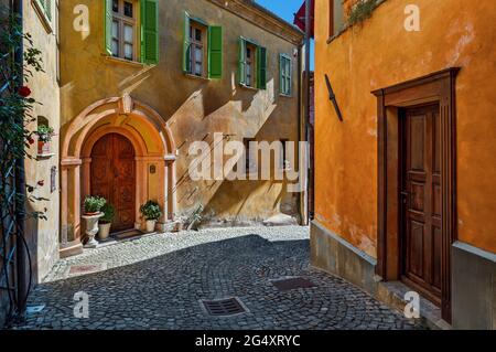 Stretta strada acciottolata tra case colorate con porte in legno d'epoca nella piccola città di Monforte d'Alba, Piemonte, Italia settentrionale. Foto Stock