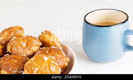 le chouquettes francesi puffs con perle di zucchero sul piatto con la tazza blu di caffè. Pasticceria Choux panetterie francesi classiche. Foto Stock