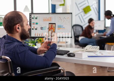 Imprenditore disabile che discute con i colleghi durante la videochiamata.dipendente seduto immobilizzato in sedia a rotelle che lavora in ufficio finanziario di affari. Foto Stock