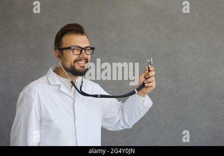 Ritratto di felice medico che tiene stetoscopio e ascolta il battito cardiaco del paziente Foto Stock