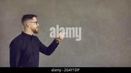 Giovane uomo caucasico in occhiali che indica da parte lo studio vuoto spazio copia Foto Stock