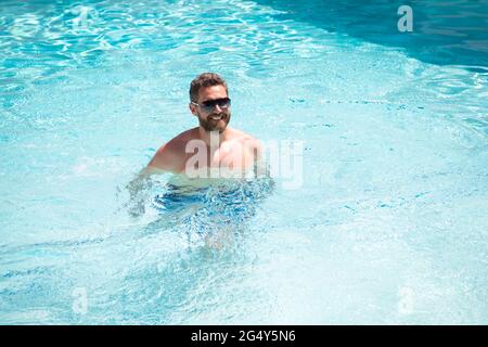 felice uomo con gli occhiali da sole godetevi relax nella piscina del resort termale durante le vacanze estive, in estate. Foto Stock