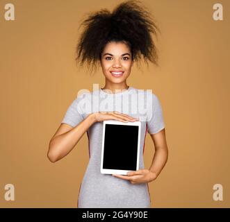 La ragazza sorridente tiene un tablet digitale. Foto di giovane ragazza vestita di abito grigio su sfondo beige Foto Stock