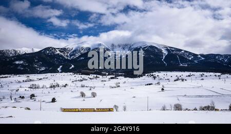 Cambredase picco nevoso vista dal villaggio di Mont-Louis in un pomeriggio invernale con il treno Jaune (treno giallo) passando (Pirenei Orientali, Francia) Foto Stock
