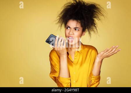 La ragazza sconvolata usa il telefono, lascia un messaggio vocale. Foto di ragazza afroamericana su sfondo giallo Foto Stock