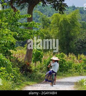 Due ragazze birmane in cappelli tradizionali in bicicletta in campagna, Myanmar Foto Stock