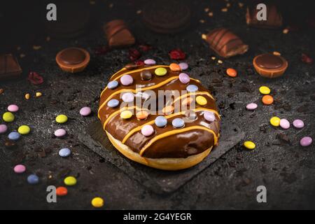Concetto di cibo dolce veloce, ciambella smaltata al cioccolato dolce decorata con caramelle firecracker Foto Stock