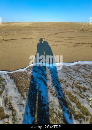 Due lunghe ombre di una coppia amorevole sulla bella spiaggia solitaria a Sete, francia durante la chiusura Foto Stock