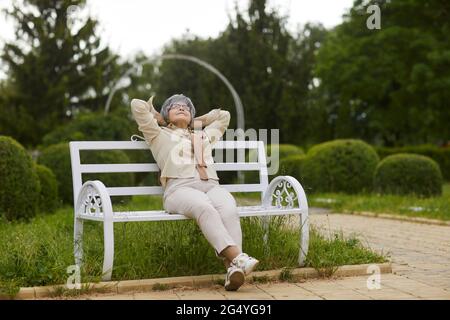 Donna anziana felice e rilassata seduta su panca di legno Godetevi una giornata di sole nel parco Foto Stock