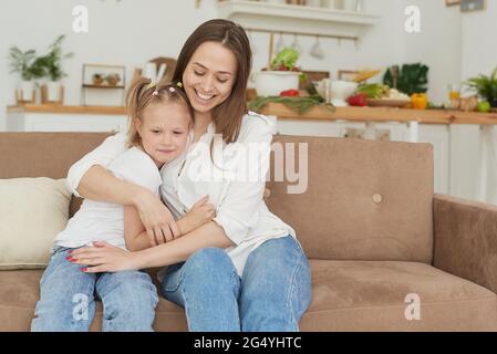 La bambina si lamenta con la madre e grida. Una giovane donna calma la figlia sul divano di casa. Foto Stock