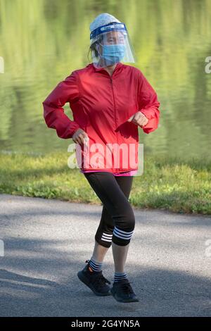 Una donna asiatica americana, probabilmente cinese, fuori per una corsa di mattina presto che indossa sia una maschera che uno scudo facciale. A Queens, New York City. Foto Stock