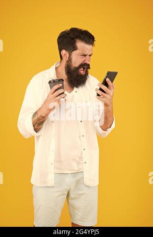 arrabbiato uomo maturo bearded gridare emozionalmente sul telefono mentre beve il caffè del mattino, esprimendo la rabbia Foto Stock