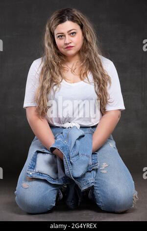 Bella donna grassa in abiti denim su sfondo grigio. Modello ragazza più grande. Foto Stock