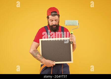 Penso che posso aiutarlo. Il caposquadra annuncia il servizio di parete che affronta. L'uomo con lo spazio di copia del bordo. hipster maturo usa l'attrezzo del rullo di vernice per la pittura Foto Stock