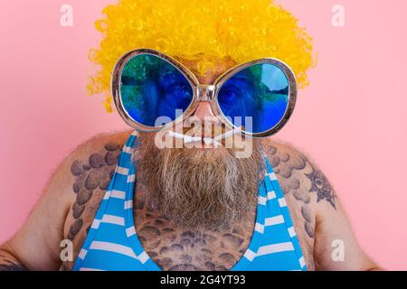 Grasso uomo serio con barba e parrucca fuma sigarette Foto Stock