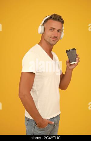 Bell'uomo ascolta la musica in cuffia bere takeaway caffè bevanda sfondo giallo, coffeeshop Foto Stock