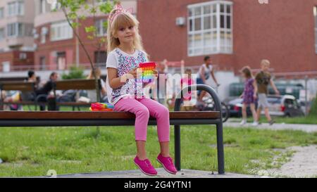 Elegante bambino ragazza spremitura preme anti-stress push pop è popolare giocattolo su panca parco giochi Foto Stock