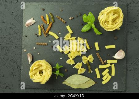 Un set di pasta e tagliatelle con spezie su un tagliere di pietra. Pasta cruda e spezie come sfondo con spazio per il testo. Vista dall'alto Foto Stock