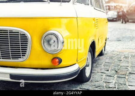 Primo piano dettaglio vista frontale del faro parte vecchia vintage giallo brillante retrò mini bus van parcheggiato nel centro della città europea su ciottoli lastricati Foto Stock