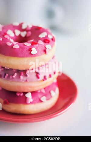 Su un piattino rosso ci sono deliziose ciambelle rosa carine con fragole ripieno e spruzzare sotto forma di cuori. Una colazione romantica con pa festivo Foto Stock