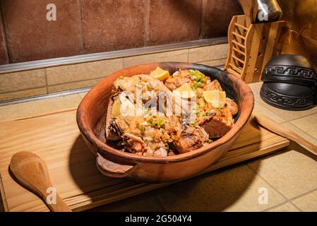 Pollo alla griglia fatto in casa con spezie tagliate a pezzi in teglia rossa in ceramica su tavola di legno. Foto Stock