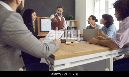 L'uomo d'affari tiene una riunione in cui i suoi dipendenti riferiscono a lui sui piani e sul lavoro svolto. Foto Stock