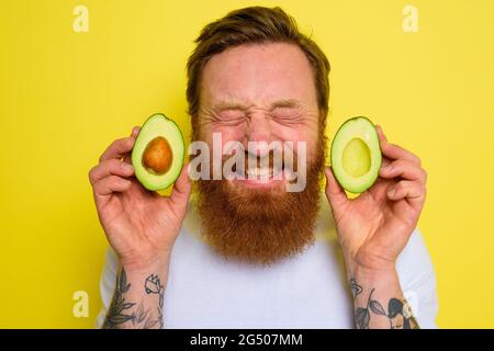 L'uomo felice con barba e tatuaggi tiene un avocado Foto Stock