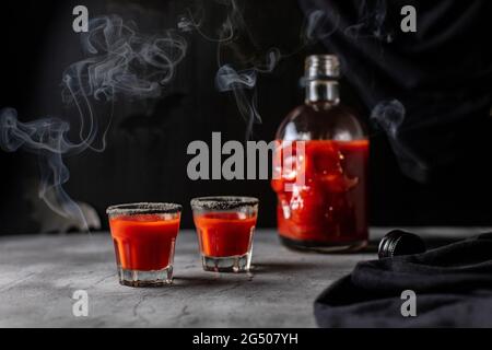 Cocktail di pomodoro in una bottiglia a forma di cranio e bicchieri con fumo. Drink per la festa di Halloween su sfondo scuro Foto Stock