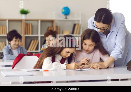 La giovane insegnante femminile aiuta la pupilla a fare un compito difficile durante la lezione in classe Foto Stock