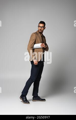 Uomo d'affari arabo in occhiali tenendo giornale su sfondo grigio Foto Stock