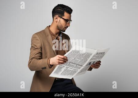 Vista laterale di uomo d'affari arabo in occhiali leggere notizie isolato su grigio Foto Stock