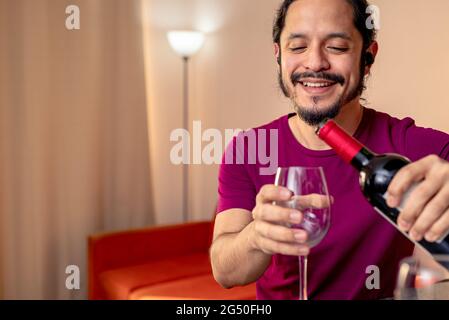 Giovane latino che beve vino rosso a casa in soggiorno Foto Stock