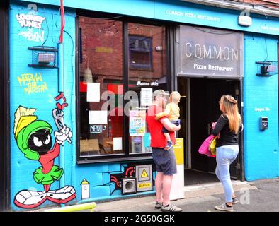 L'uomo, la donna e il bambino stanno accanto a un'immagine del personaggio dei cartoni animati marziani Marvin, parte di un percorso artistico Looney Tunes che ha aperto a Manchester, Inghilterra, Regno Unito. Il percorso segnerà il film Space Jam: A New Legacy che sarà presto nei cinema a Manchester. Le immagini dei cartoni animati appaiono in 12 località a Manchester. Questo su Edge Street. Foto Stock