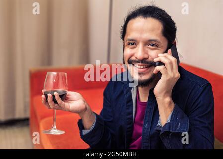 Giovane latino che beve vino rosso a casa in soggiorno Foto Stock