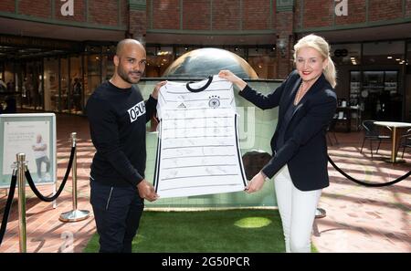 Amburgo, Germania. 24 Giugno 2021. David Odonkor, ex calciatore nazionale tedesco, consegna una maglia di calcio della nazionale tedesca a Sylvia Nielius, manager di centro Hansaviertel, come parte di un evento benefico nel centro commerciale Hanseviertel. I proventi saranno devoluti alla Fördergemeinschaft Kinderkrebs-Zentrum Hamburg e.V. (Associazione di sostegno al Centro per il cancro dei bambini di Amburgo). Credit: Daniel Reinhardt/dpa/Alamy Live News Foto Stock