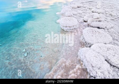 Sabbia completamente coperta di sale cristallino sulla riva del Mar Morto, acque turchesi blu vicino - scenario tipico alla spiaggia di Ein Bokek, Israele Foto Stock