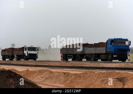 Autocarri che trasportano carichi lungo una strada in costruzione. Foto Stock