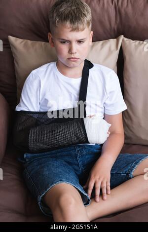 Ragazzo triste con un braccio rotto e ferite sulla gamba. Gesso sulla mano di un bambino. Foto Stock