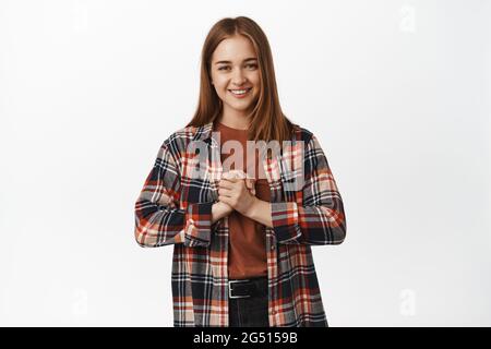 Giovane donna sorridente tenendo le mani aggrappate vicino petto speranzoso, chiedendo qualcosa, sperando, pregando di avere possibilità, in piedi su sfondo bianco Foto Stock