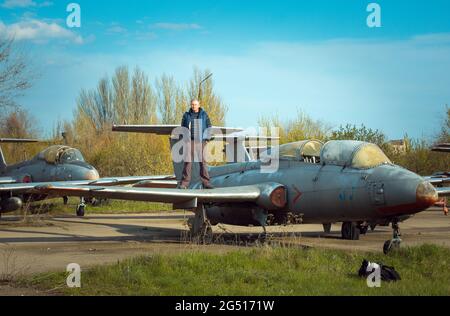 Un uomo di mezza età vicino a un vecchio piano sovietico abbandonato. Aereo sul campo del vecchio aeroporto. Foto Stock